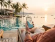 A hotel guest by a beachfront pool in Nusa Dua checking phone directions to a nearby spa, with coconut palm trees in the background